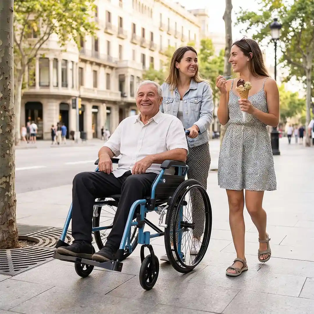 Chicas pasean por la calle mientras una de ellas lleva a su padre en la silla de ruedas de aluminio de peso ligero y de fácil maniobrabilidad dortomedical