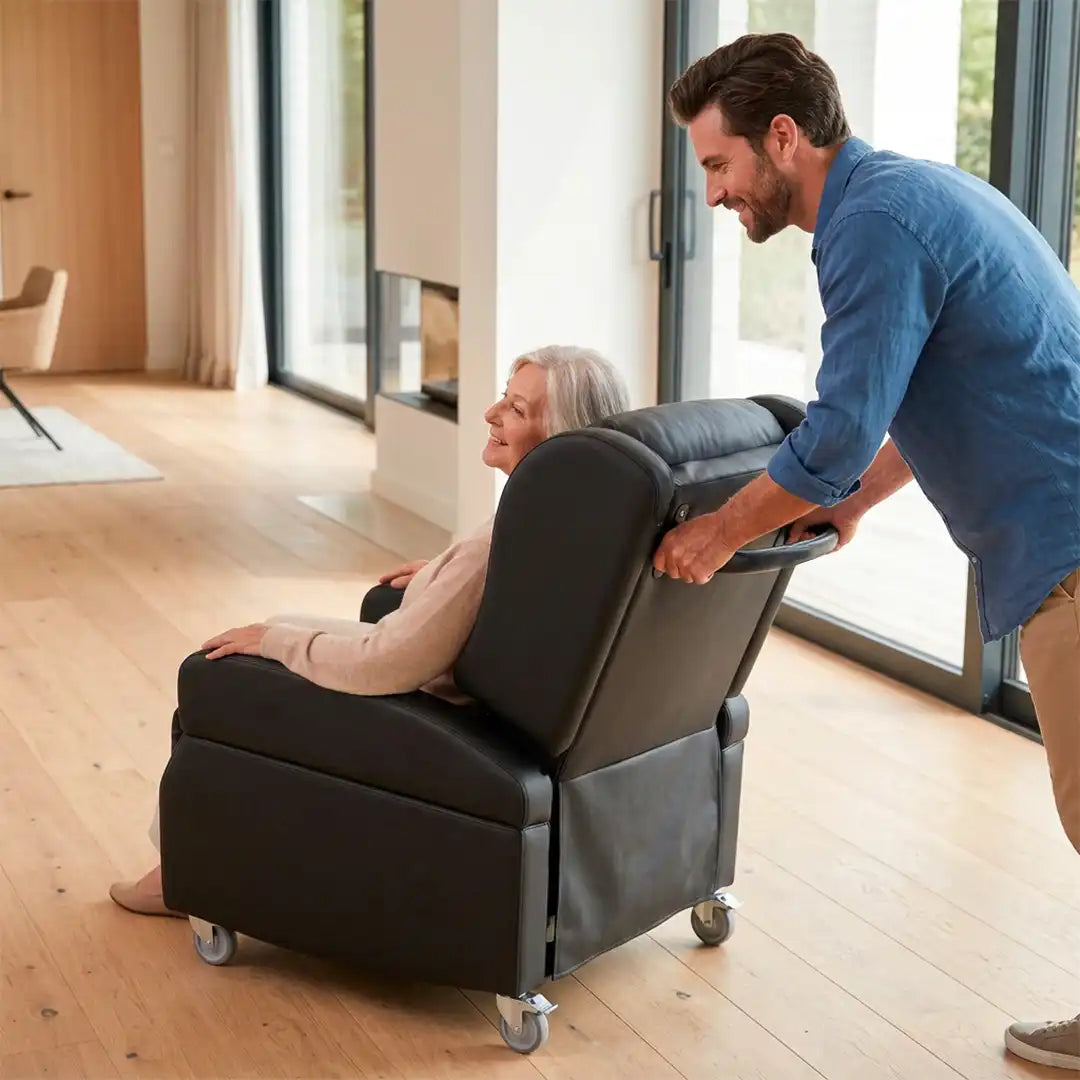Un joven traslada el sillón fácilmente gracias al asa de empuje ergonómica y las ruedas con freno, facilitando la movilidad del paciente dentro de casa dortomedical