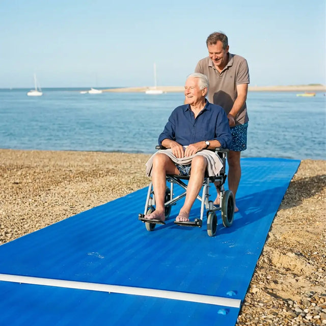 Usuario pasando con silla de ruedas por pasarela de playa resistente al agua salada y a los rayos UV para una mayor durabilidad dortomedical